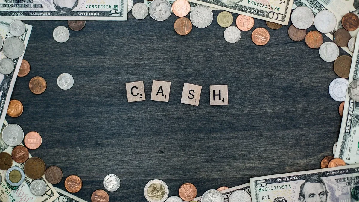 A collection of US currency and coins arranged around the word "CASH" on a dark wooden surface.