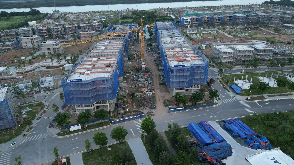 A construction site with multiple buildings under development, featuring blue tarps and scaffolding, situated in a suburban area with a body