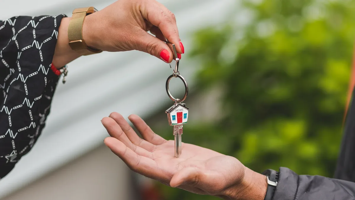 A person handing over a set of keys attached to a keychain shaped like a house.