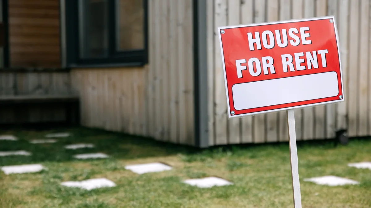 A red and white "House for Rent" sign in front of a house.